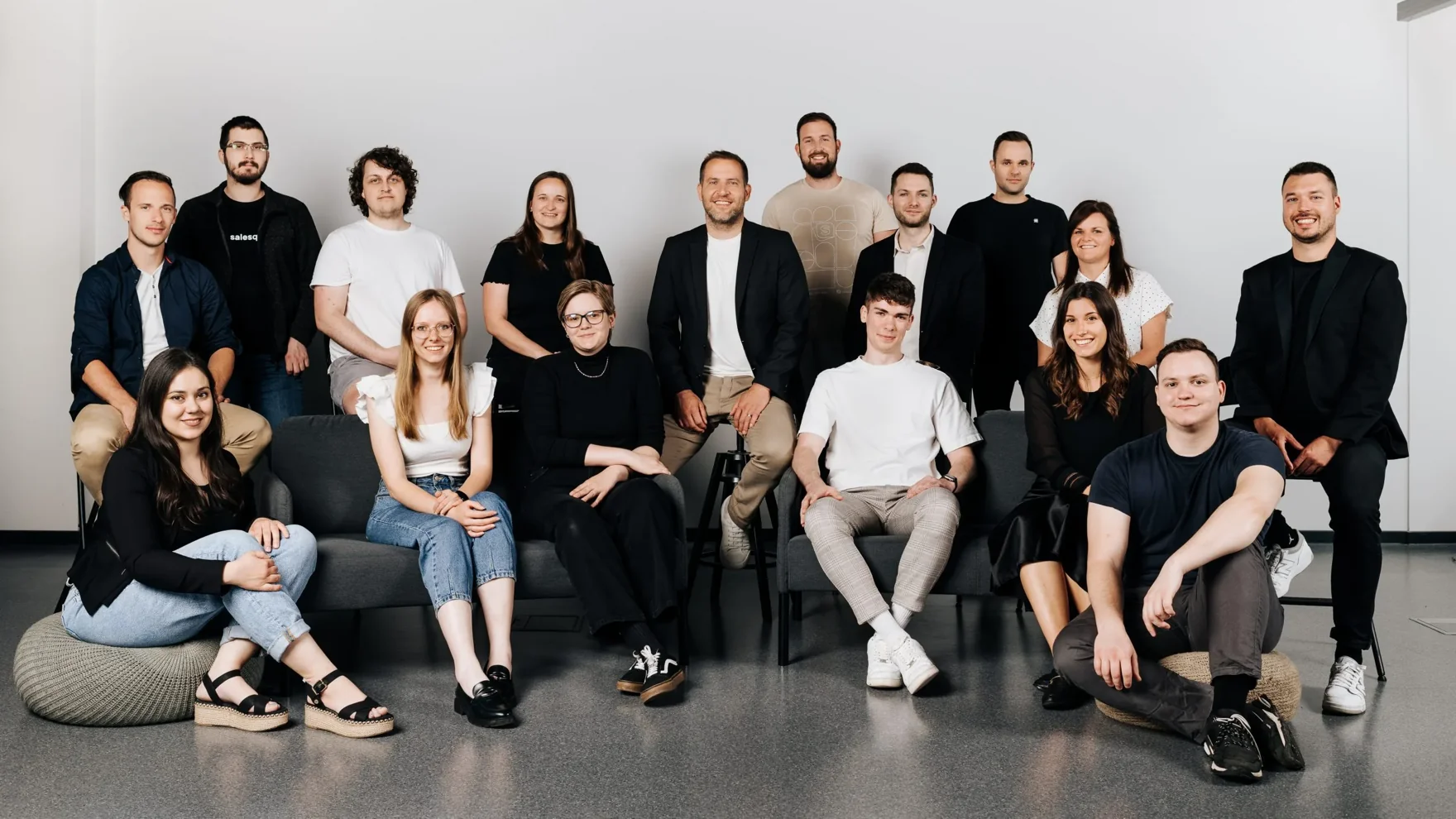 The SaleSqueze team. Seventeen people seated together in a bright office: the founders and the build, design, and customer-success teams behind 160+ live configurators.