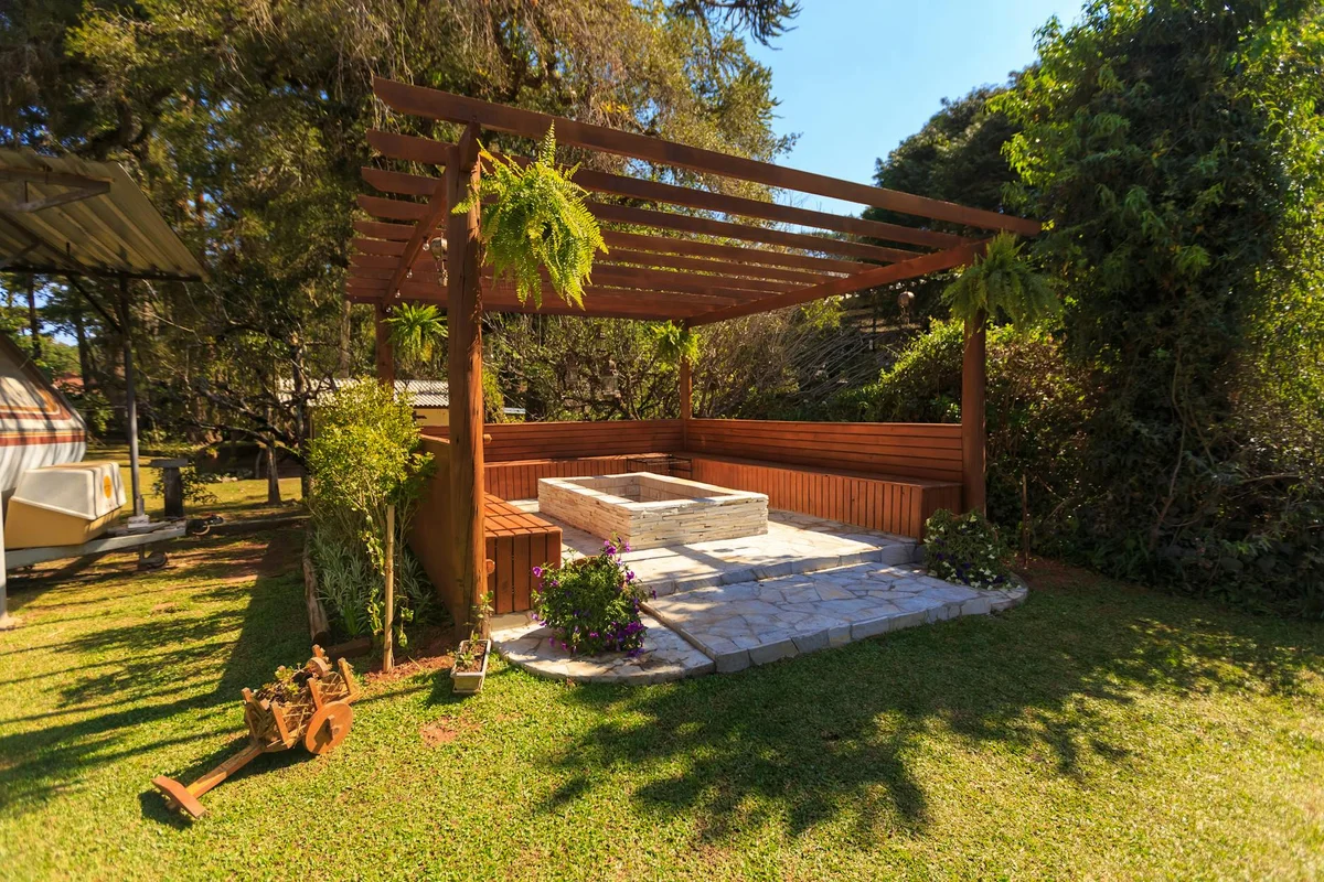 A finished wooden pergola in a residential garden, with built-in bench seating and a stone patio underneath.