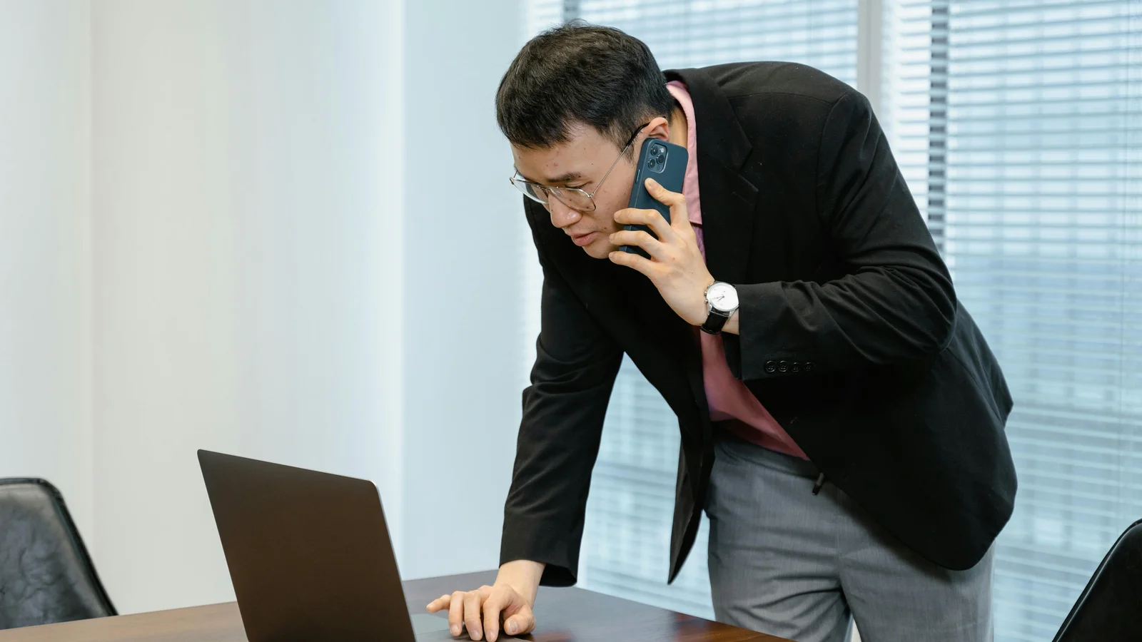 A salesperson at a desk multitasking with a laptop open in front of him and a smartphone to his ear, working a live quote conversation in real time.