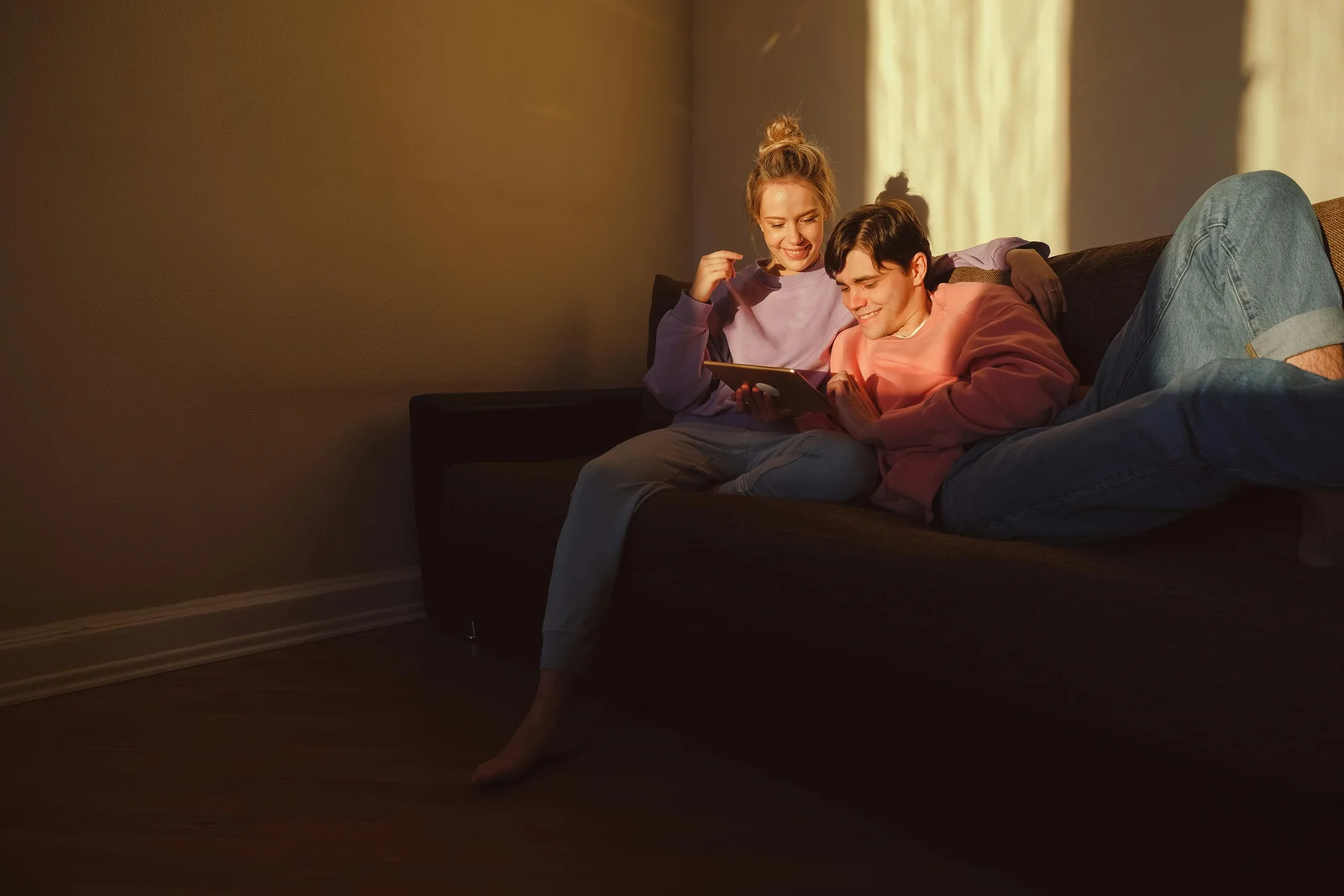 A couple sitting on a sofa together using a tablet in warm evening light, browsing through a configurator on a quiet weeknight.