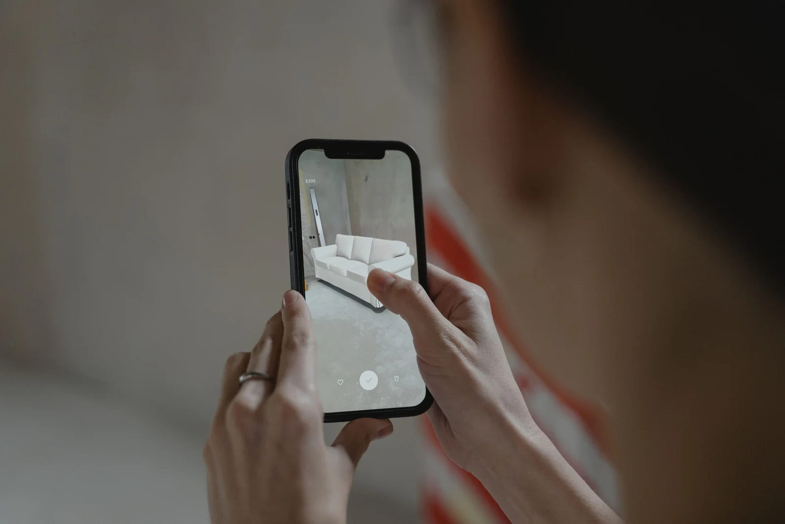 A shopper holding a phone that shows a white sofa placed into their own living room through an augmented reality product app.