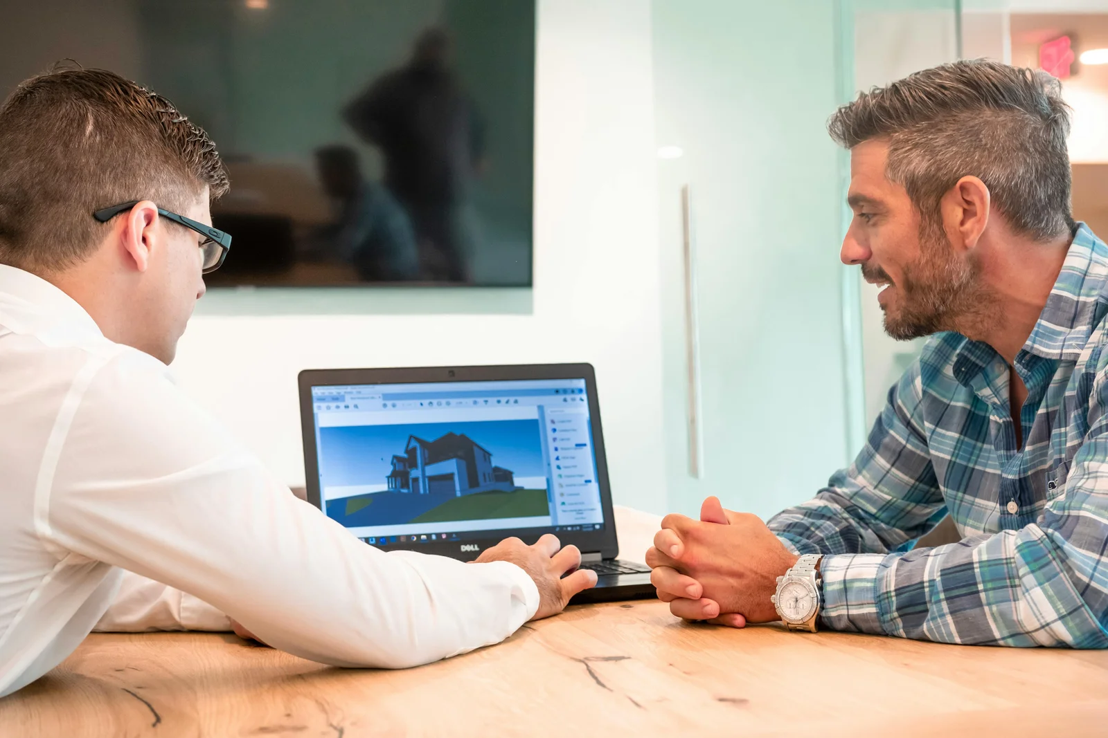 Two people at a table looking at a 3D building design on a laptop screen, talking it through.