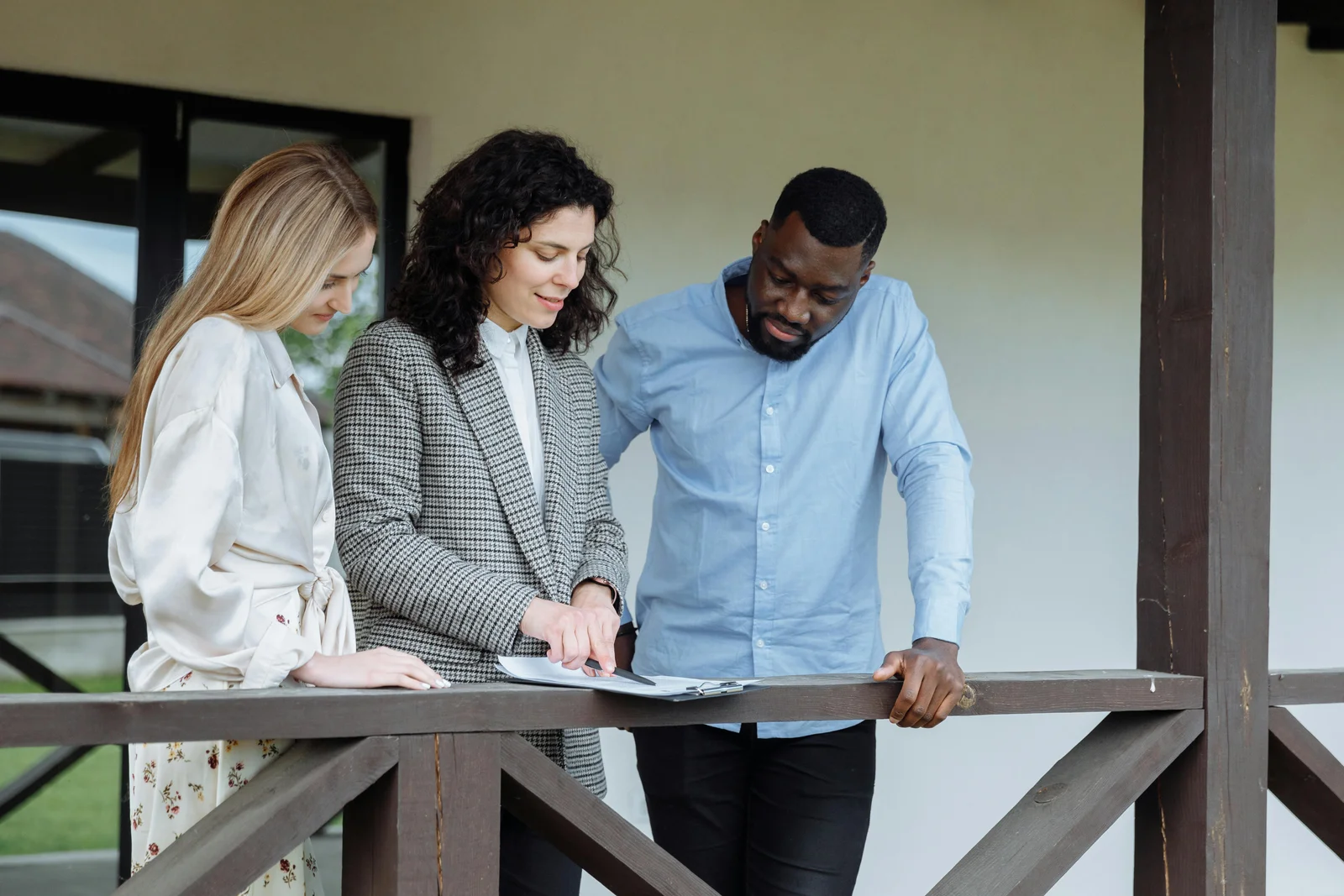 An outdoor living dealer walking a couple through a printed quote on a porch, the document open between them as they ask about the bottom-line price.