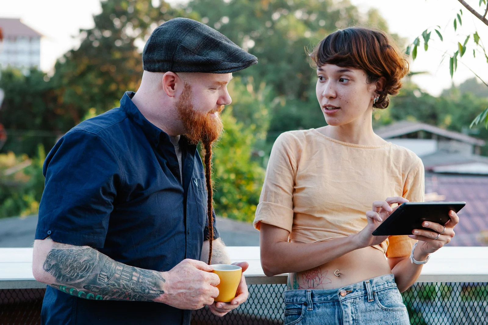 A man and a woman on a sunny summer terrace, the woman holding a tablet as the two talk through a design together.