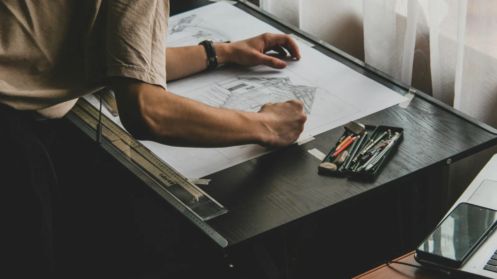Close-up of an architect drafting a building design on a desk with a pencil, ruler, and trace paper, in the slow manual style a pergola seller still uses on a Sunday evening.