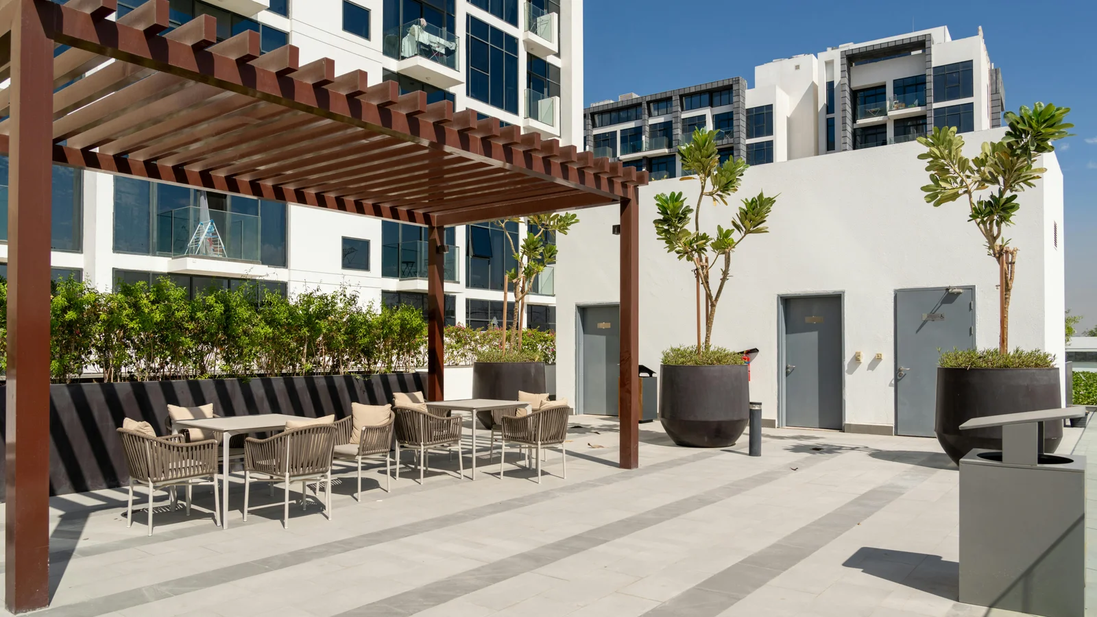 A sleek modern outdoor terrace at golden hour with a louvered aluminium pergola over a lounge seating area, looking out over a city skyline.