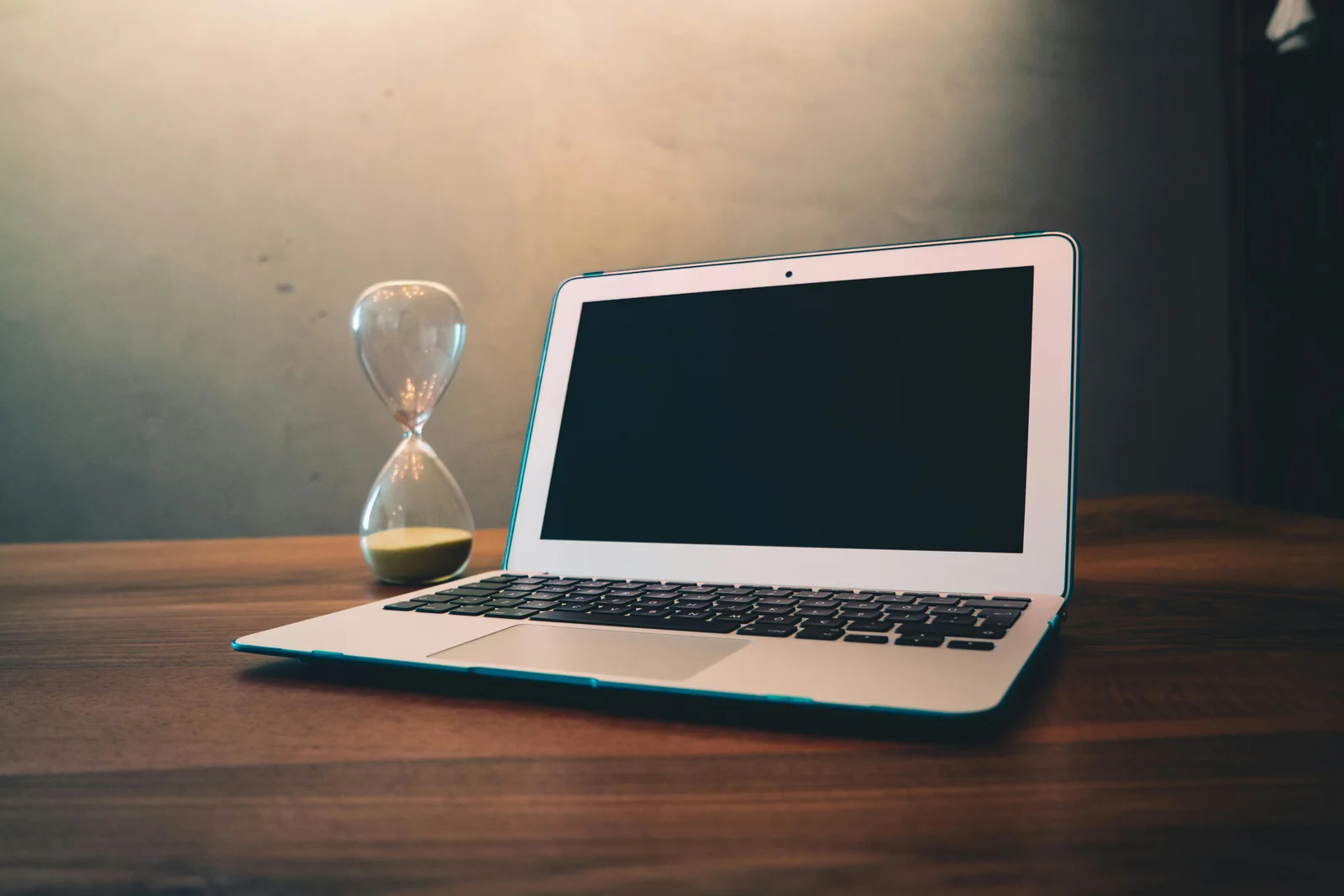 A laptop and an hourglass sitting side by side on a wooden desk, the visual shorthand for the 24-hour clock running against a custom pergola quote.