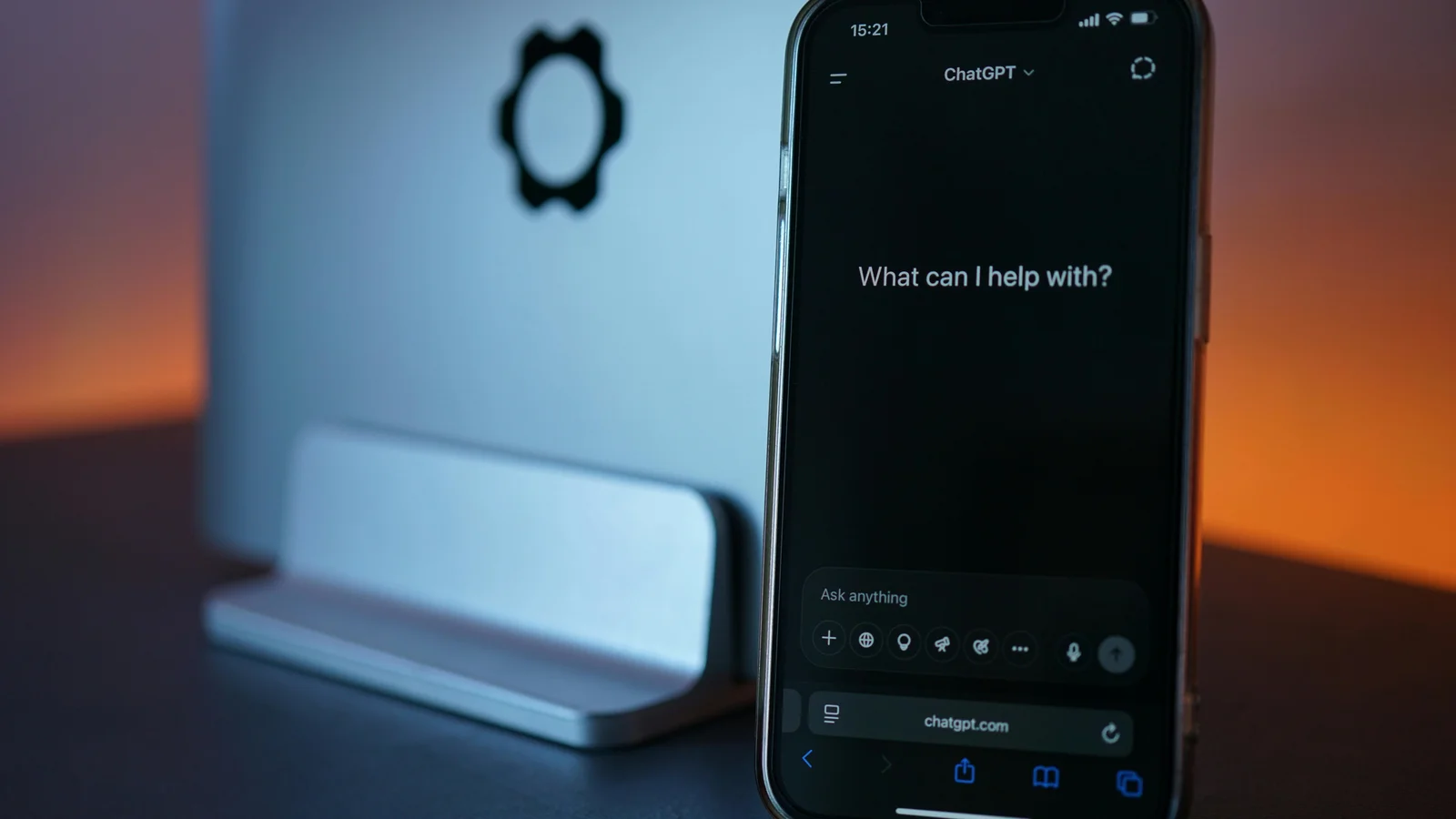 A smartphone in the foreground showing a chat interface, with a laptop in the background, the two devices framed side by side on a workspace.