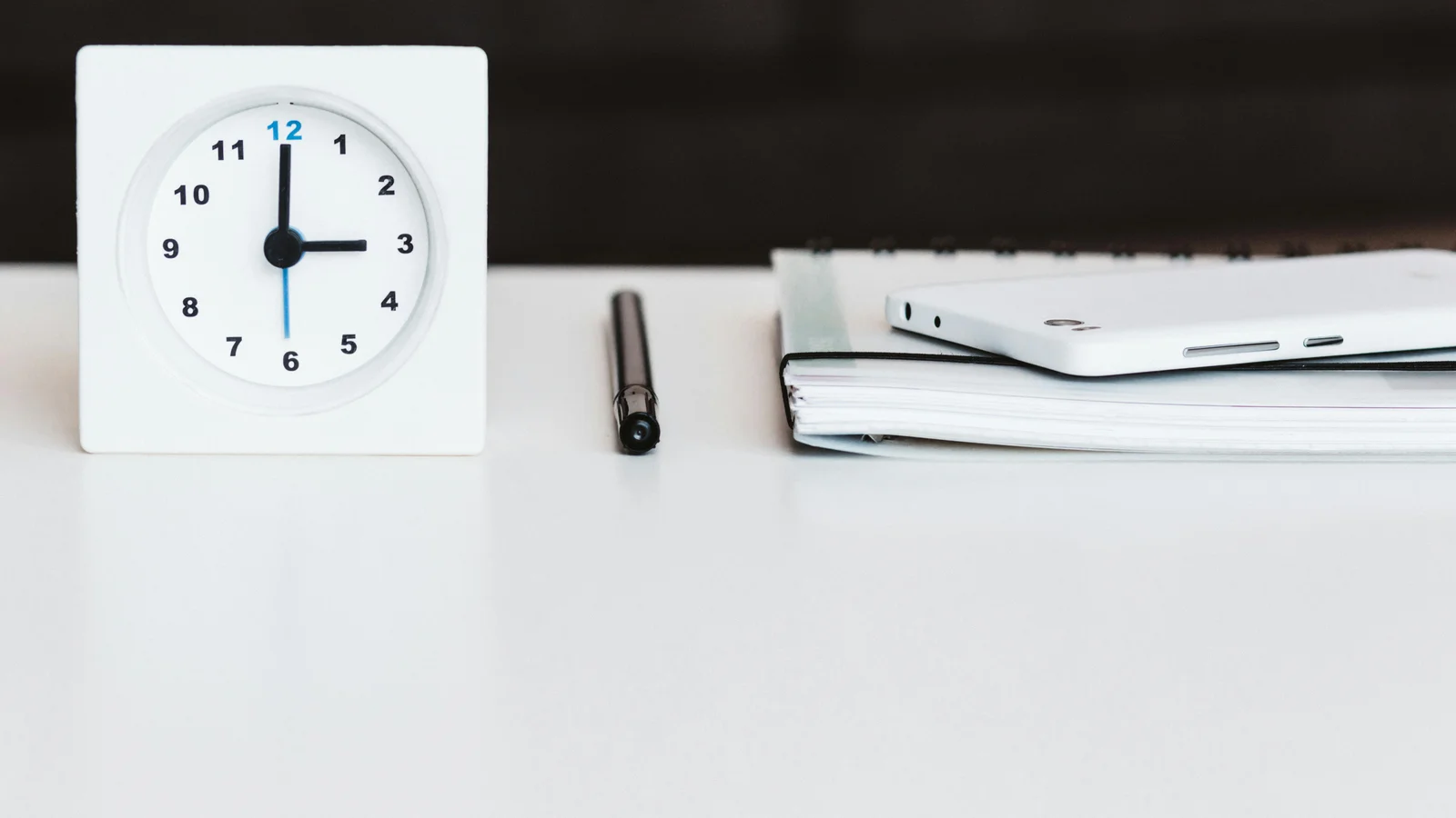 A minimalist office desk at dawn with a clock, a smartphone, a pen, and a notebook, the scene of a buyer waiting on a reply.