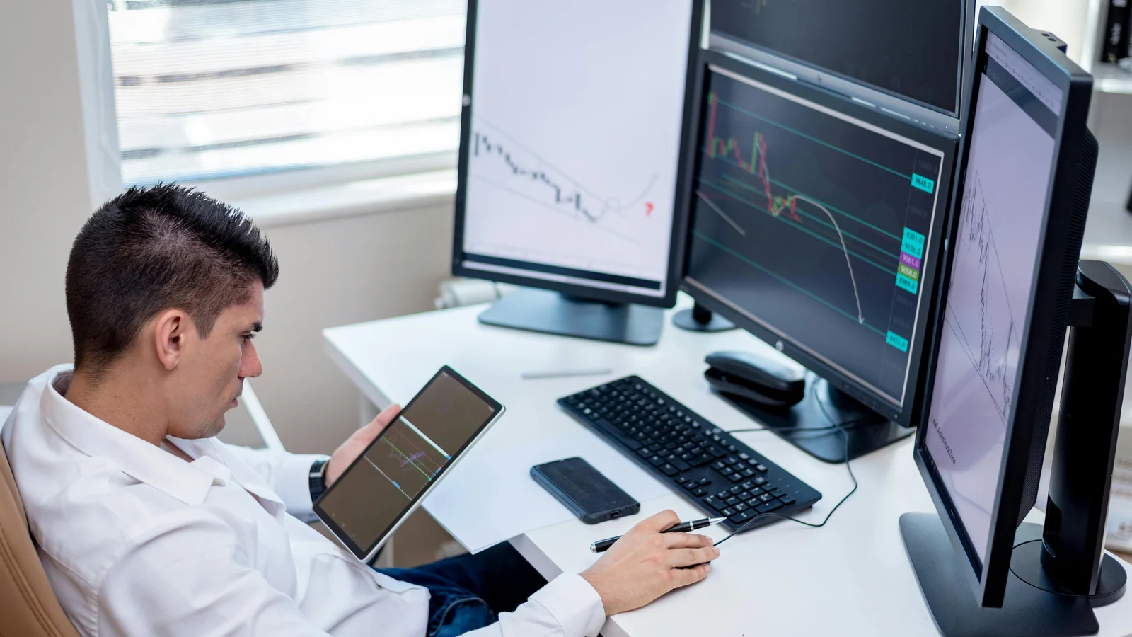 A sales operator at a busy office workstation with multiple screens of charts and a tablet in hand, the kind of desk where most of the week disappears into repetitive translation work.
