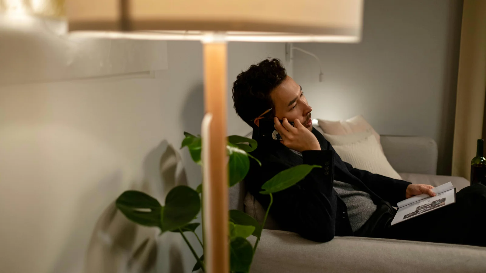 A buyer on a sofa under a warm lamp in the evening, phone in one hand and a notebook in the other, weighing whether to reply to a quote.